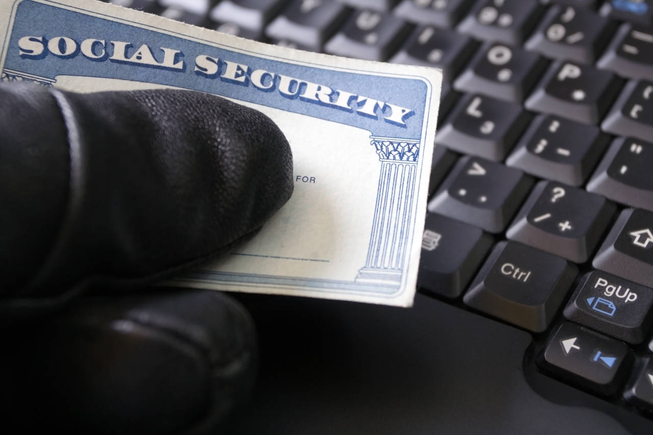 Hand with leather gloves holding a paper that reads Social Security, keyboard in the background.