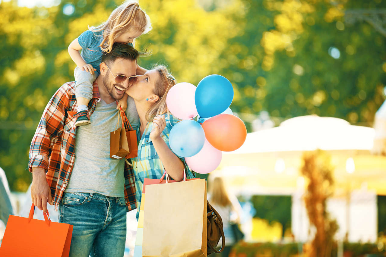 A man holding a little girl on his shoulder while a woman kisses him on the cheek